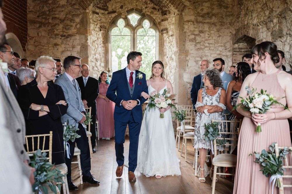Wedding ceremony takes place in historic stone chapel with gothic window and guests lining the aisle.