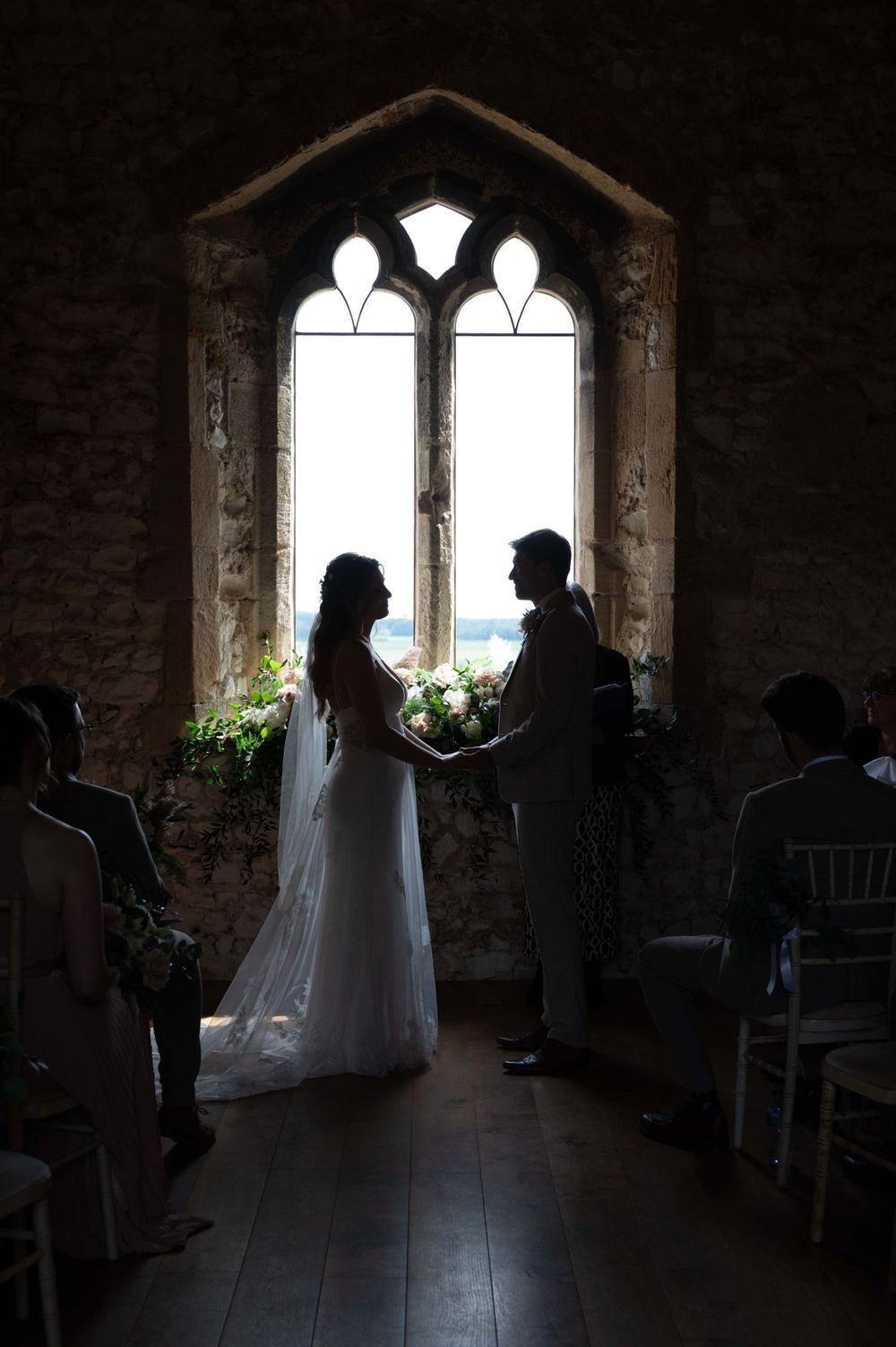 A silhouetted couple exchanging vows in front of a gothic church window during an intimate wedding ceremony.