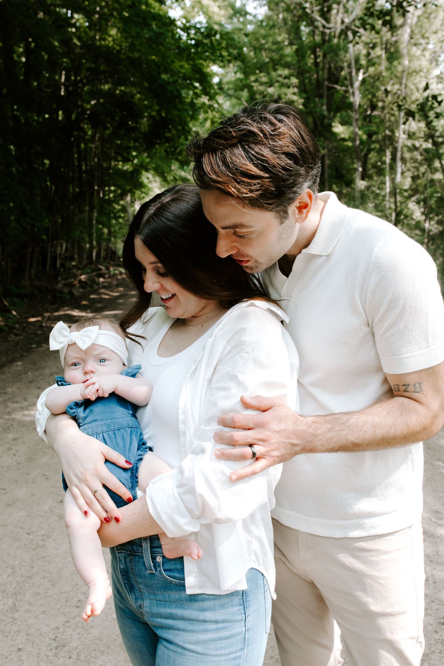 Family of three sharing tender moment on outdoor path surrounded by greenery.