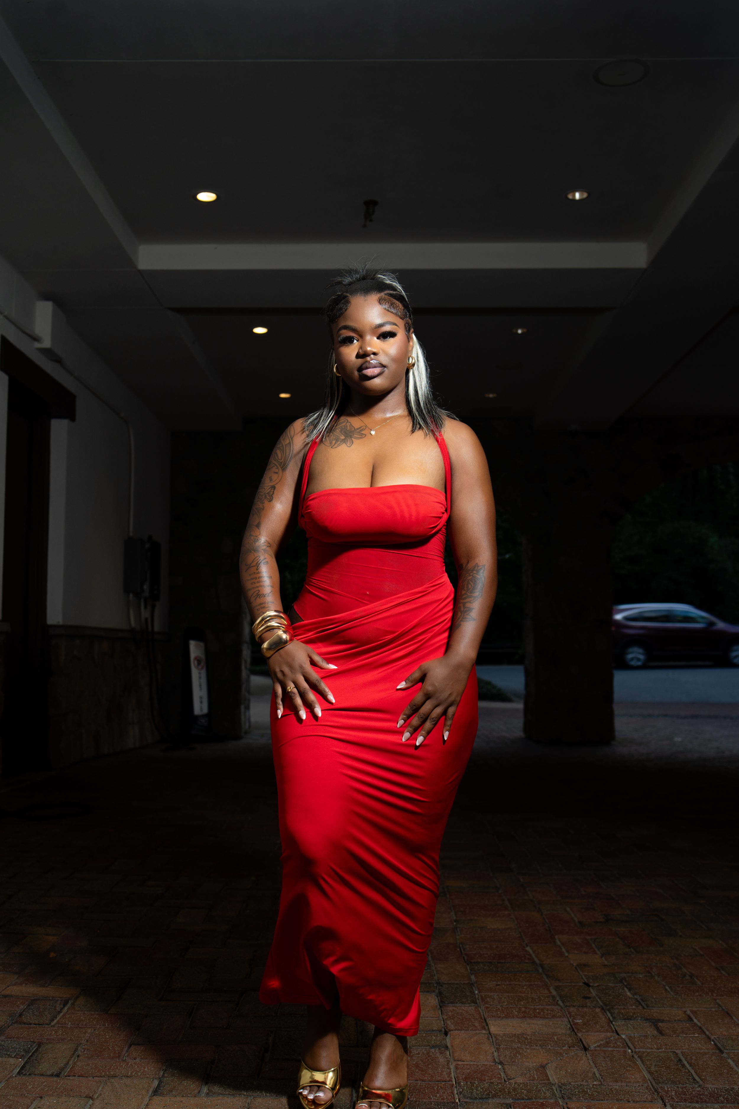 Striking portrait of a person in a fitted red evening dress posing confidently in a dimly lit hallway.