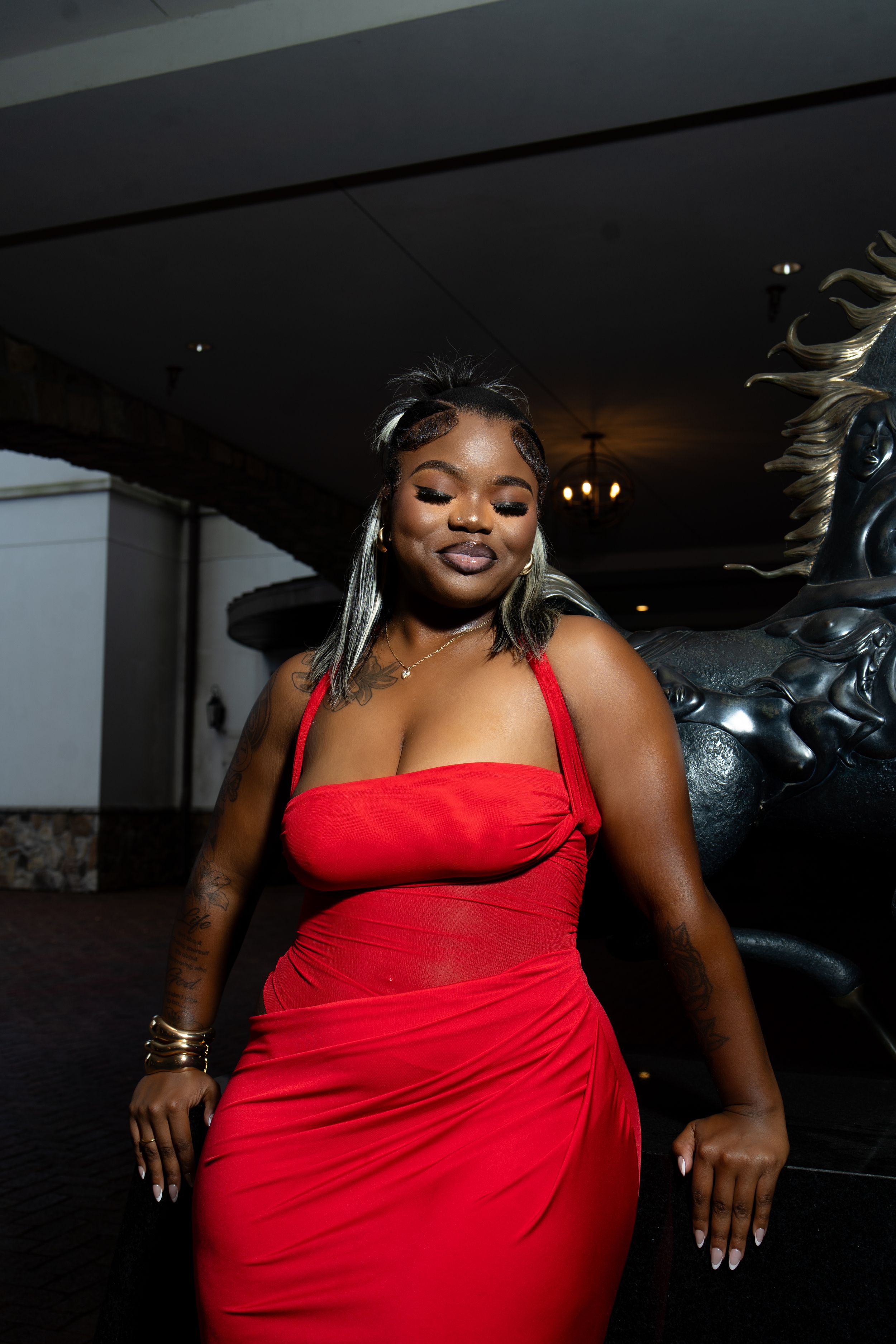 A person in a vibrant red dress poses confidently against a dark background during a photoshoot.