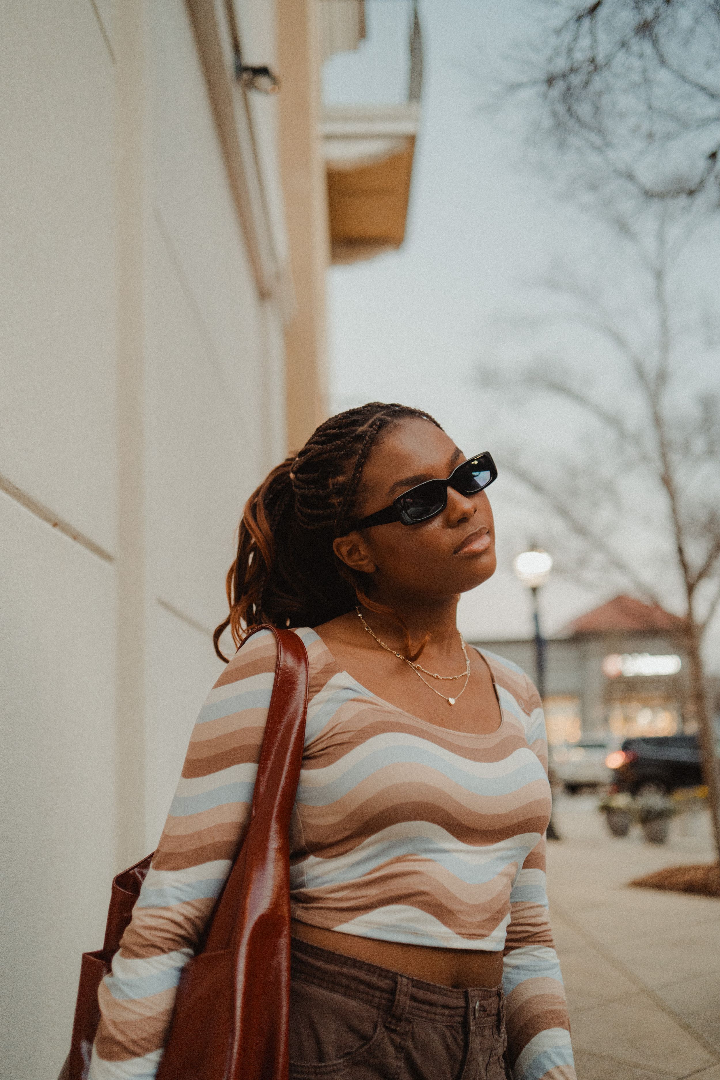Someone in sunglasses and a striped top carries a brown bag while walking downtown.