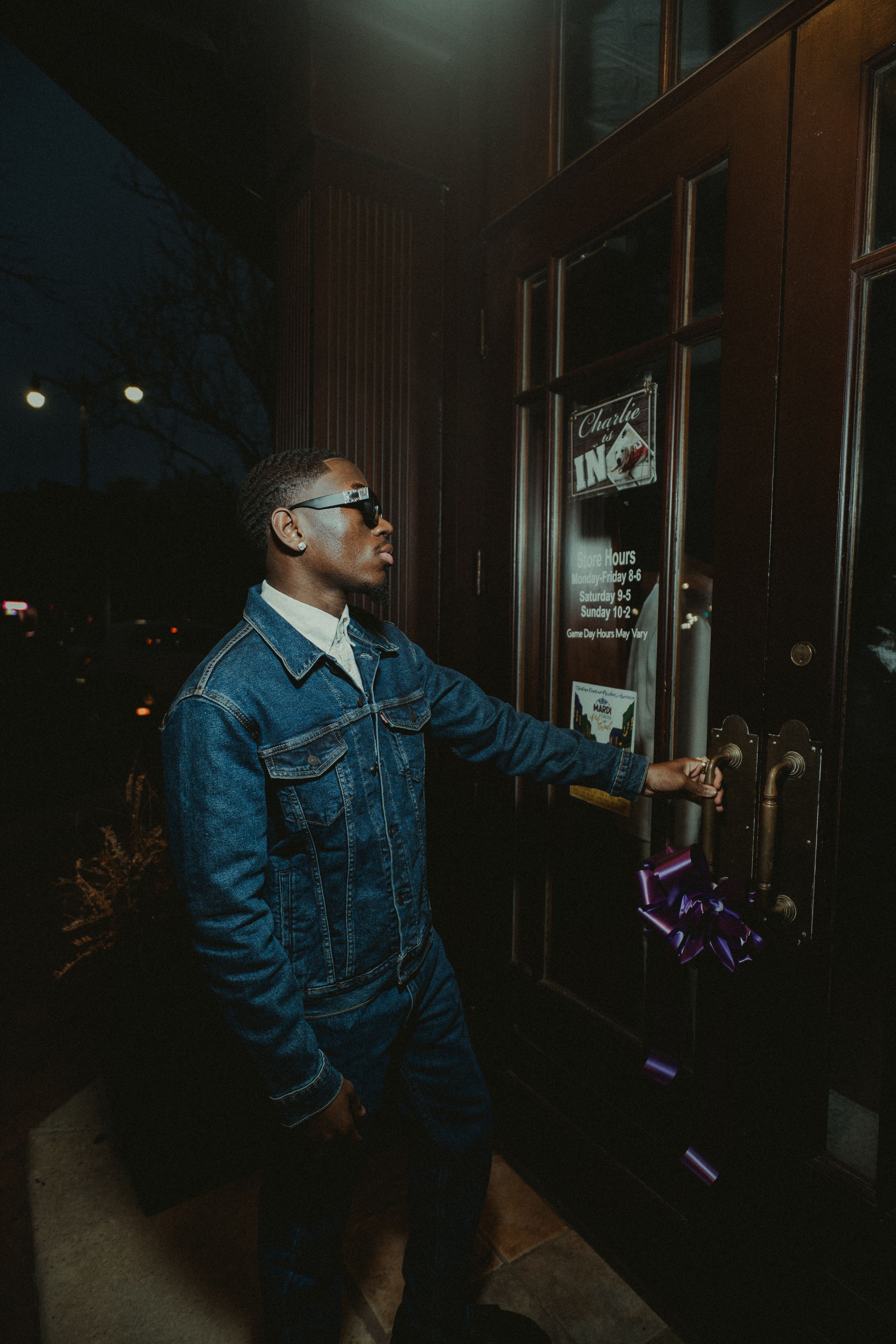 Person in denim jacket and sunglasses dancing in a dark room with purple lighting effects.