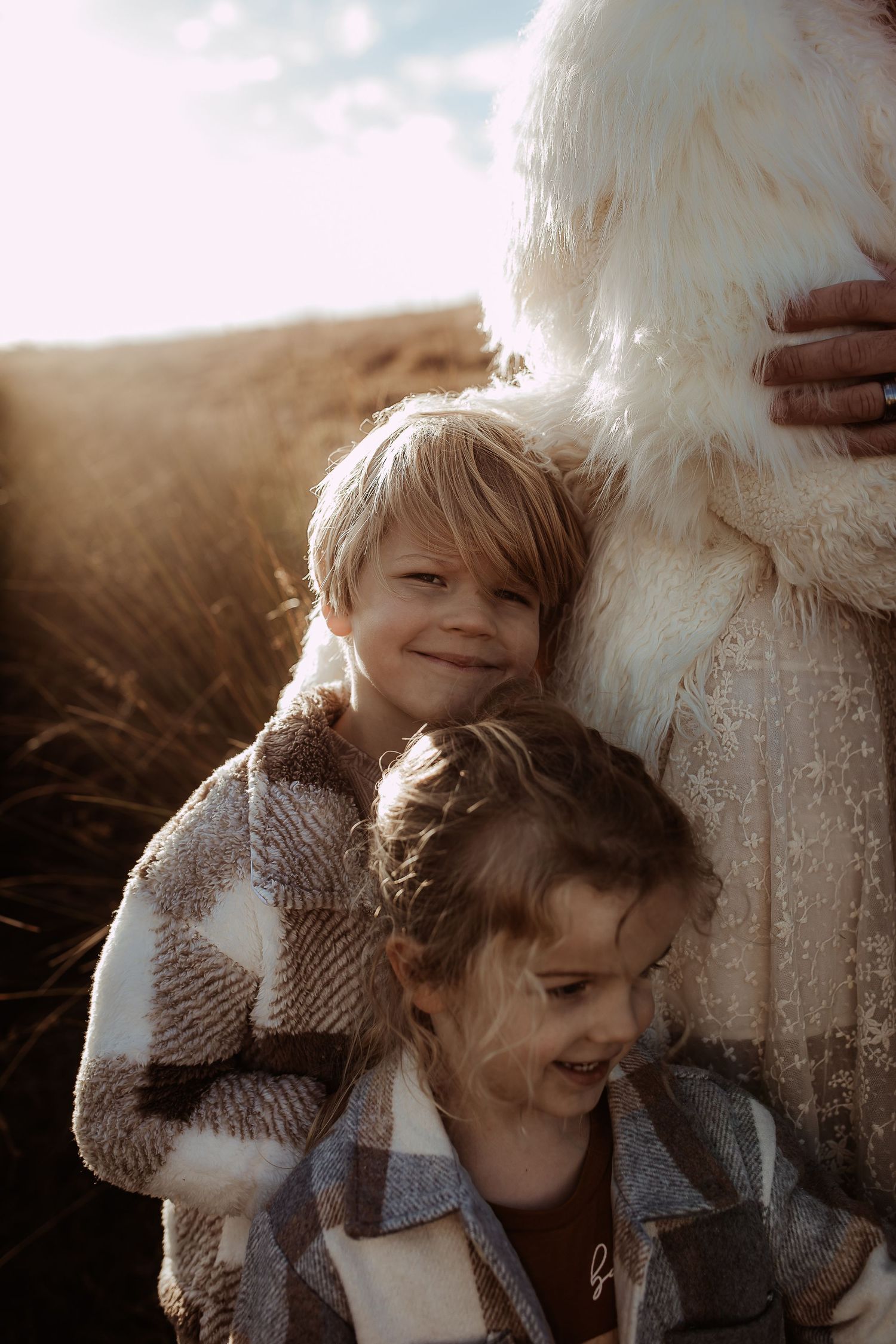Two children snuggle close in cozy sweaters during a golden hour photoshoot.