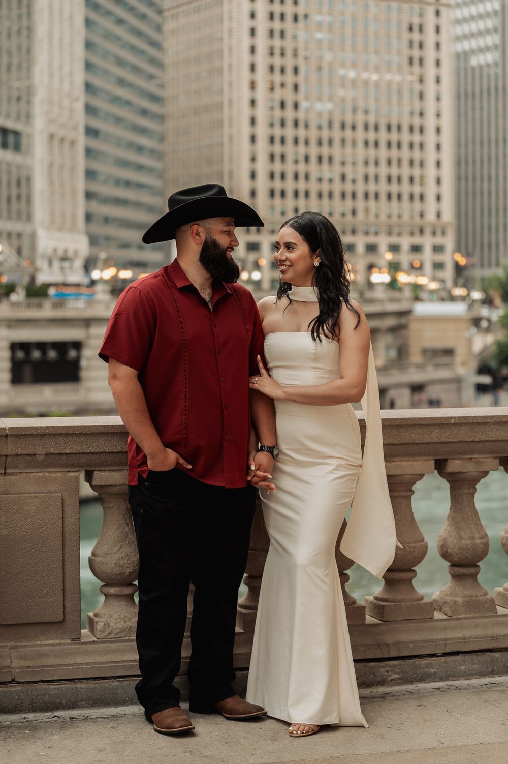 Couple posing along Chicago Riverwalk with urban skyline and architecture in background.