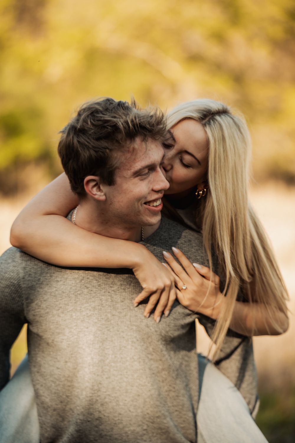 A couple shares an intimate embrace outdoors during a fall photoshoot with golden bokeh lighting in the background.