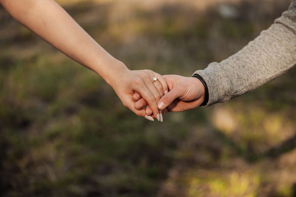 Close-up shot of hands exchanging wedding rings during an outdoor ceremony in natural sunlight.