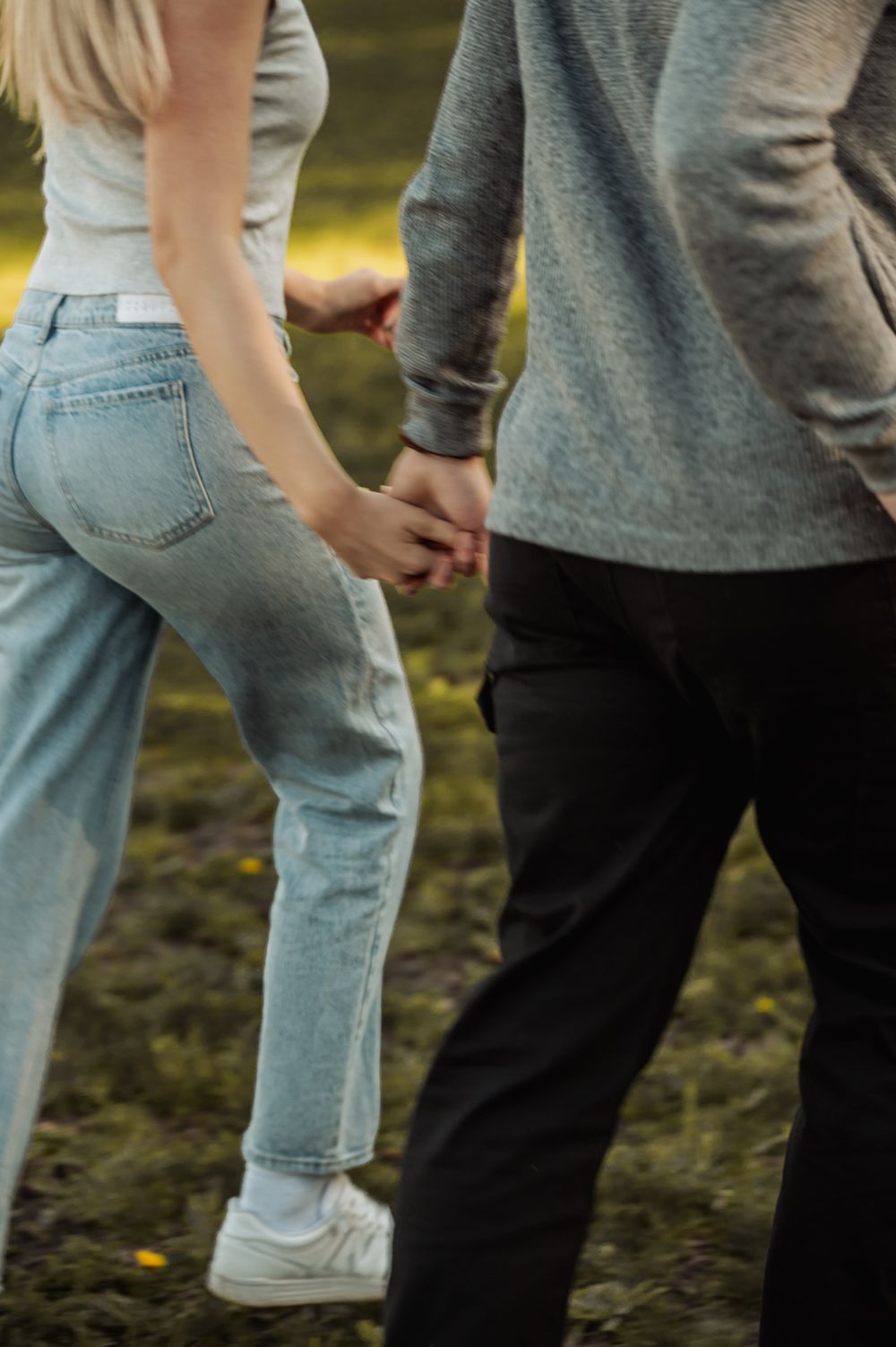 Close-up view of people's legs and feet standing in casual jeans and sneakers on mossy ground outdoors.
