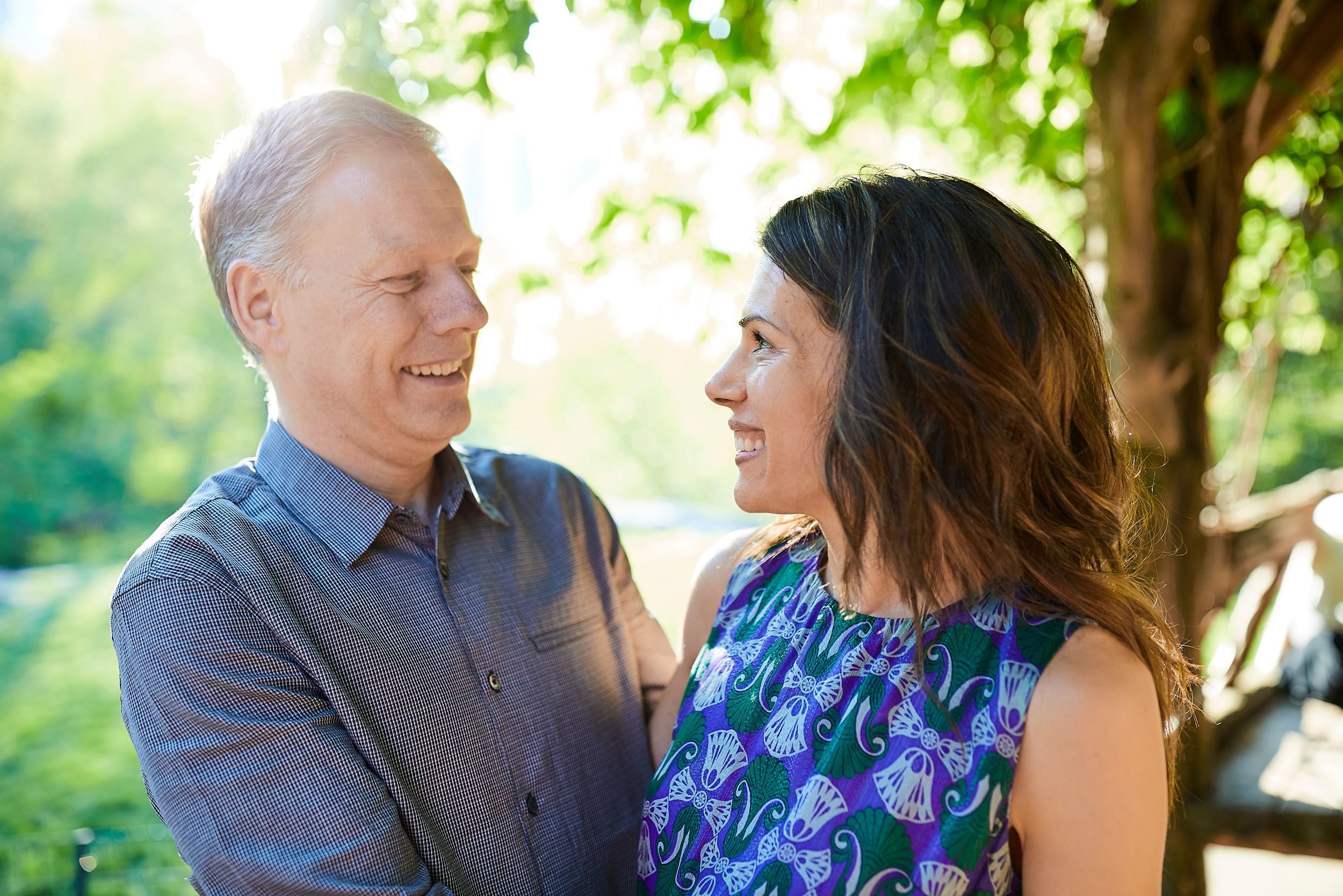 A sunny outdoor engagement portrait with lush greenery and natural sunlight.