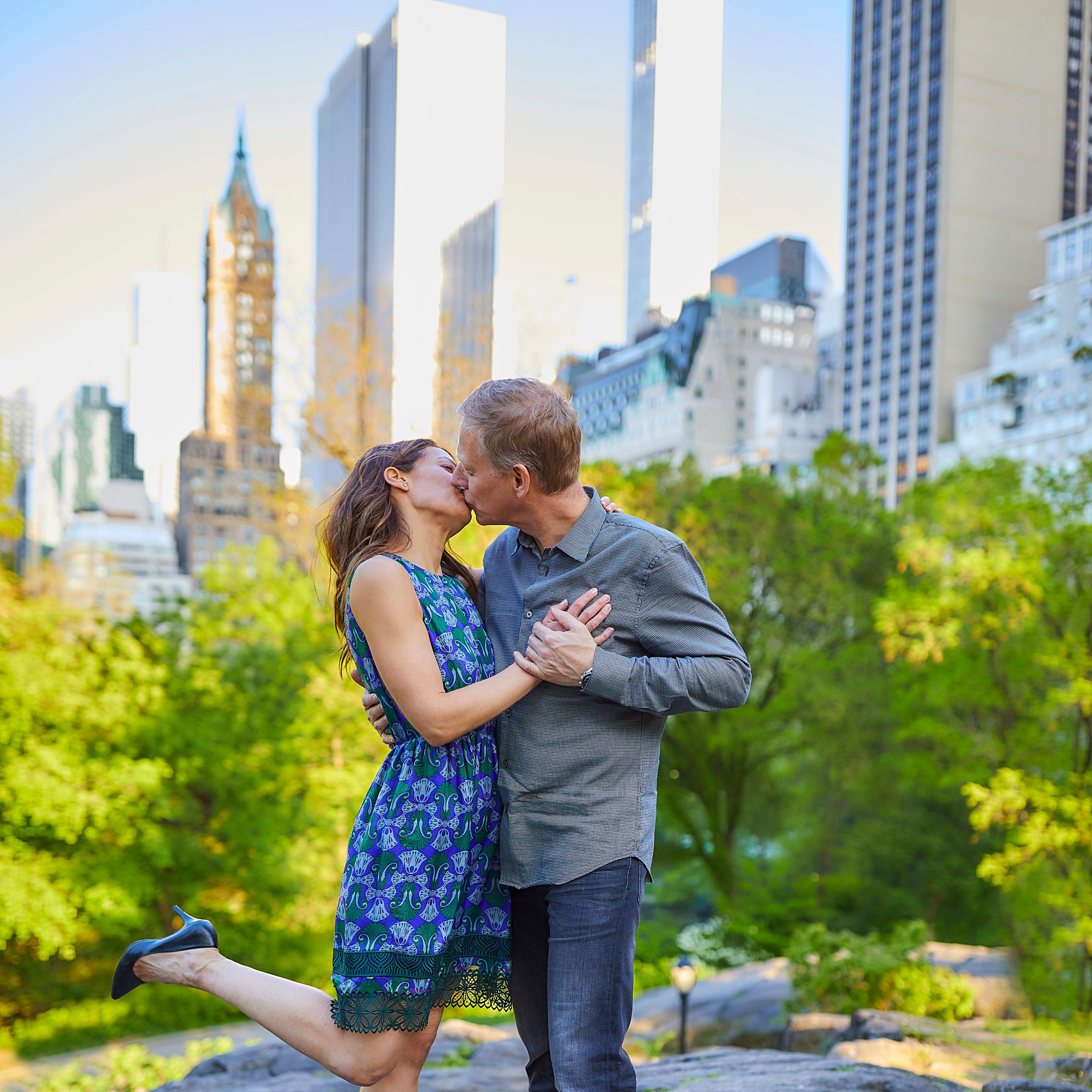 A romantic engagement photo in Central Park with the NYC skyline and spring foliage in the background.