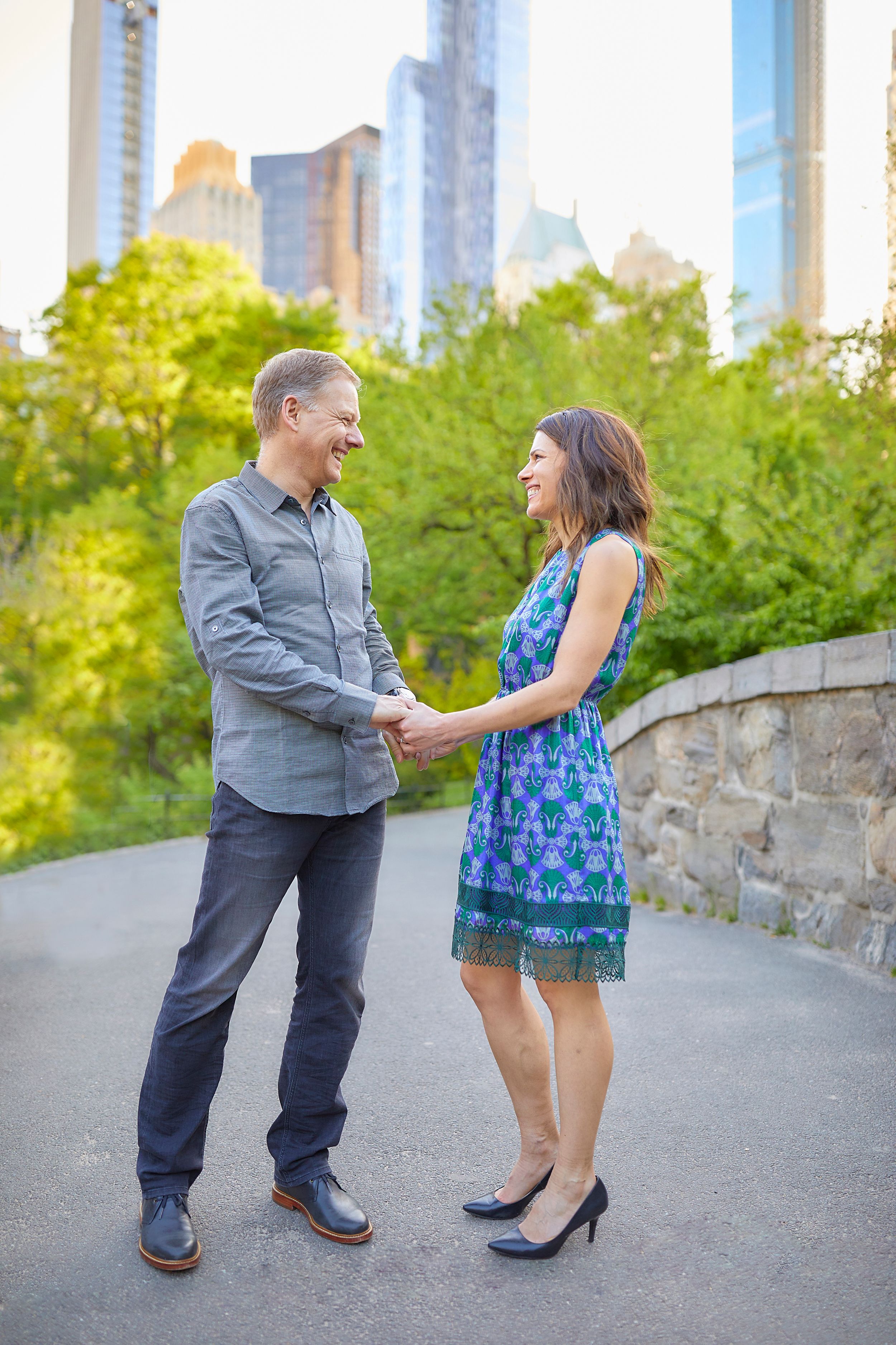 Central Park NYC sunny engagement photo in an urban park with skyscrapers and greenery in the background.