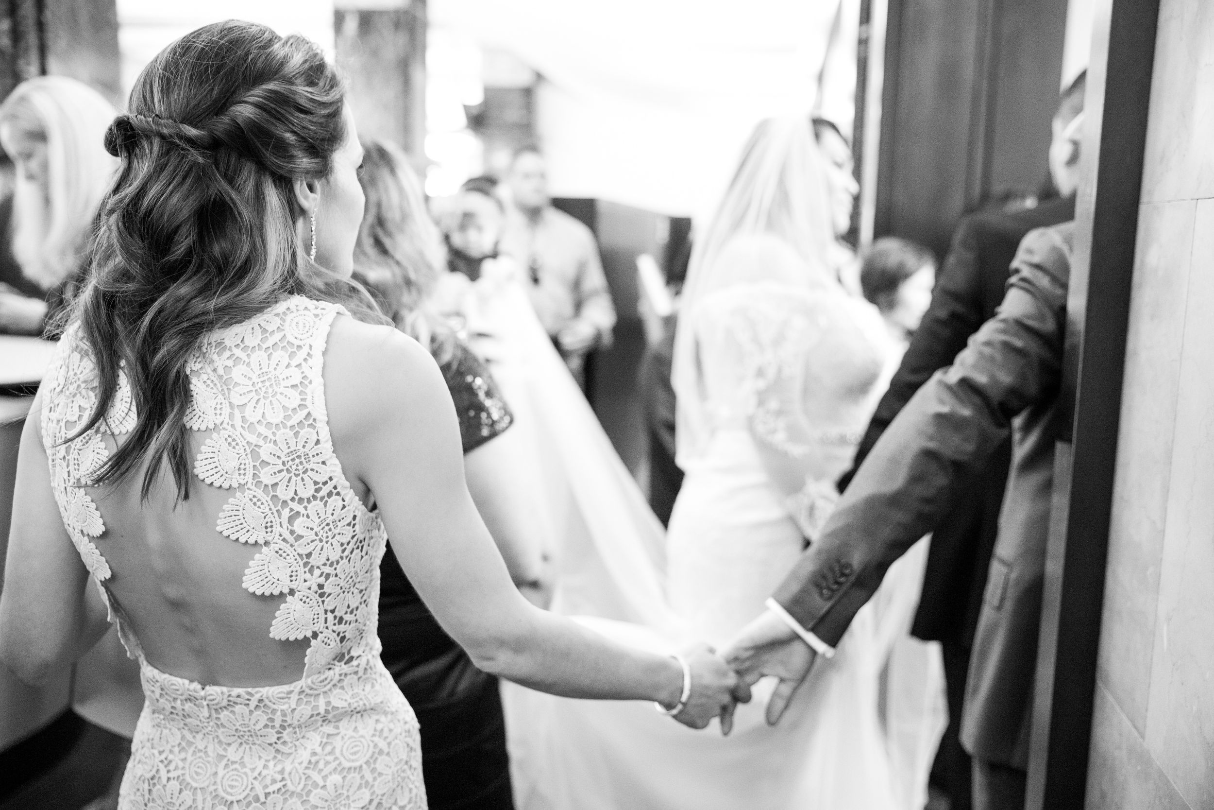 Black and white wedding photo showing elegant lace dress details and joined hands.