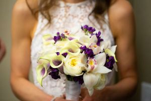 An elegant bridal bouquet featuring white calla lilies, yellow roses and purple flowers wrapped in white ribbon.