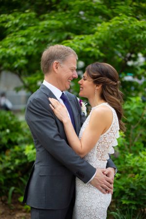 A romantic wedding couple embracing outdoors surrounded by lush green foliage.
