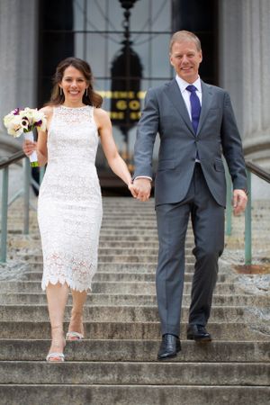 A couple descends stone steps outside a grand building after their wedding ceremony.
