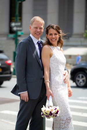 A happy wedding couple poses on a city street with the bride holding a floral bouquet.