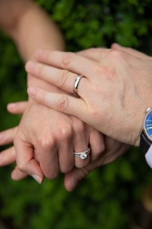 Close-up of newlyweds' hands showing their wedding rings against a green background.