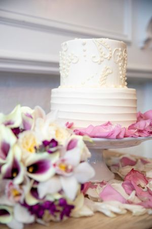 White wedding cake with delicate piping decoration surrounded by purple and pink flower petals.