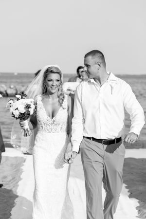 A romantic beach wedding ceremony with a couple smiling and walking on white sand with ocean views in the background.