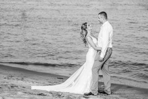 A romantic black and white beach wedding portrait with waves crashing in the background.