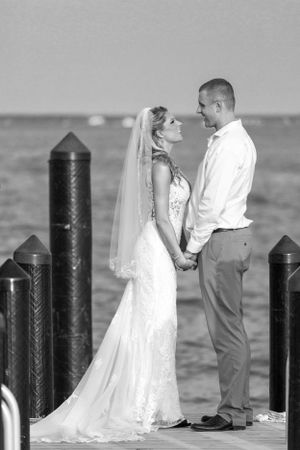 A beautiful wedding photo on a dock with wooden posts and water in the background.