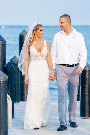 A couple strolls along a waterfront dock during their wedding photoshoot.