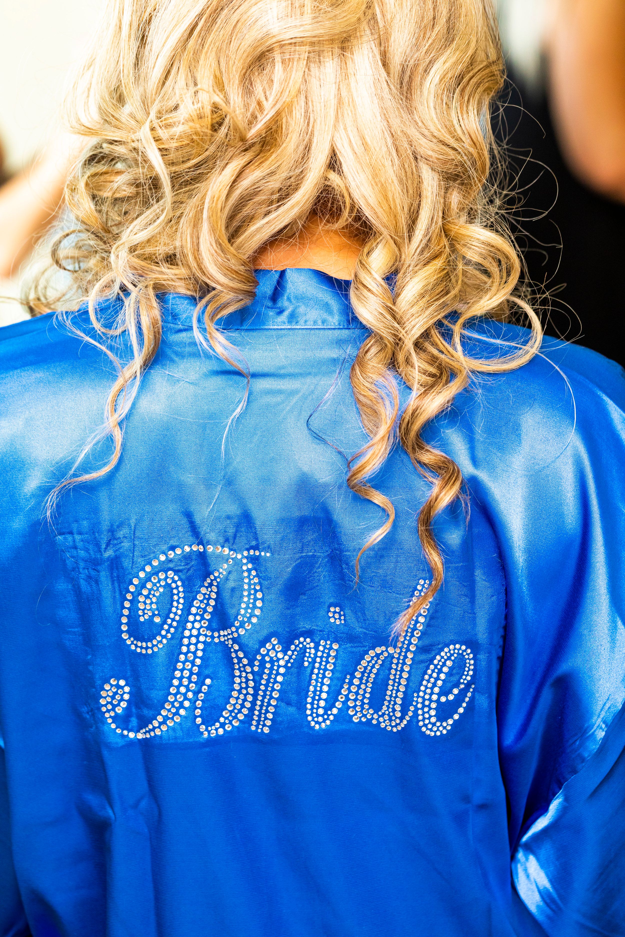 A blue satin robe with rhinestone 'Bride' text on the back.
