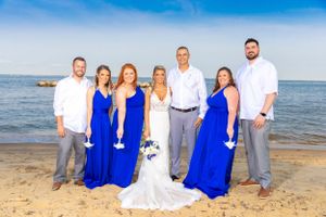 Wedding party in blue and white attire poses for formal beach photo.