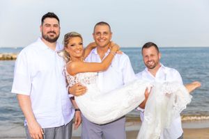 Beach wedding group photo with groomsmen carrying bride.