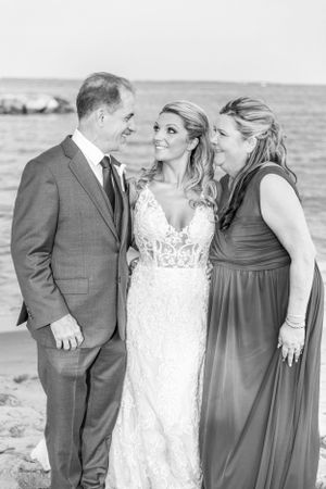 A tender black and white beach wedding moment with three people sharing smiles and laughter.
