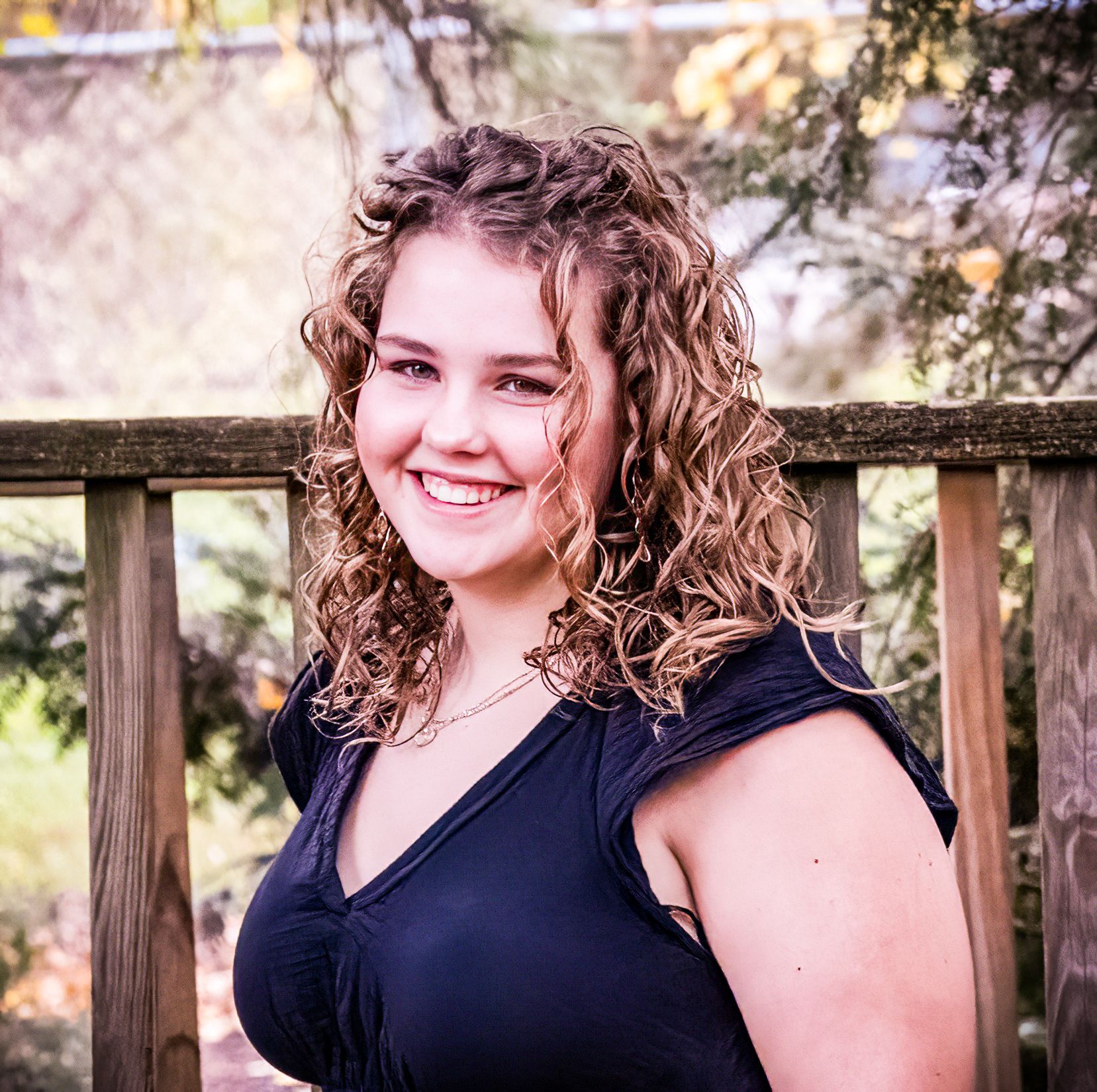 Outdoor portrait featuring navy blue top against wooden deck railing with natural background.
senior photography