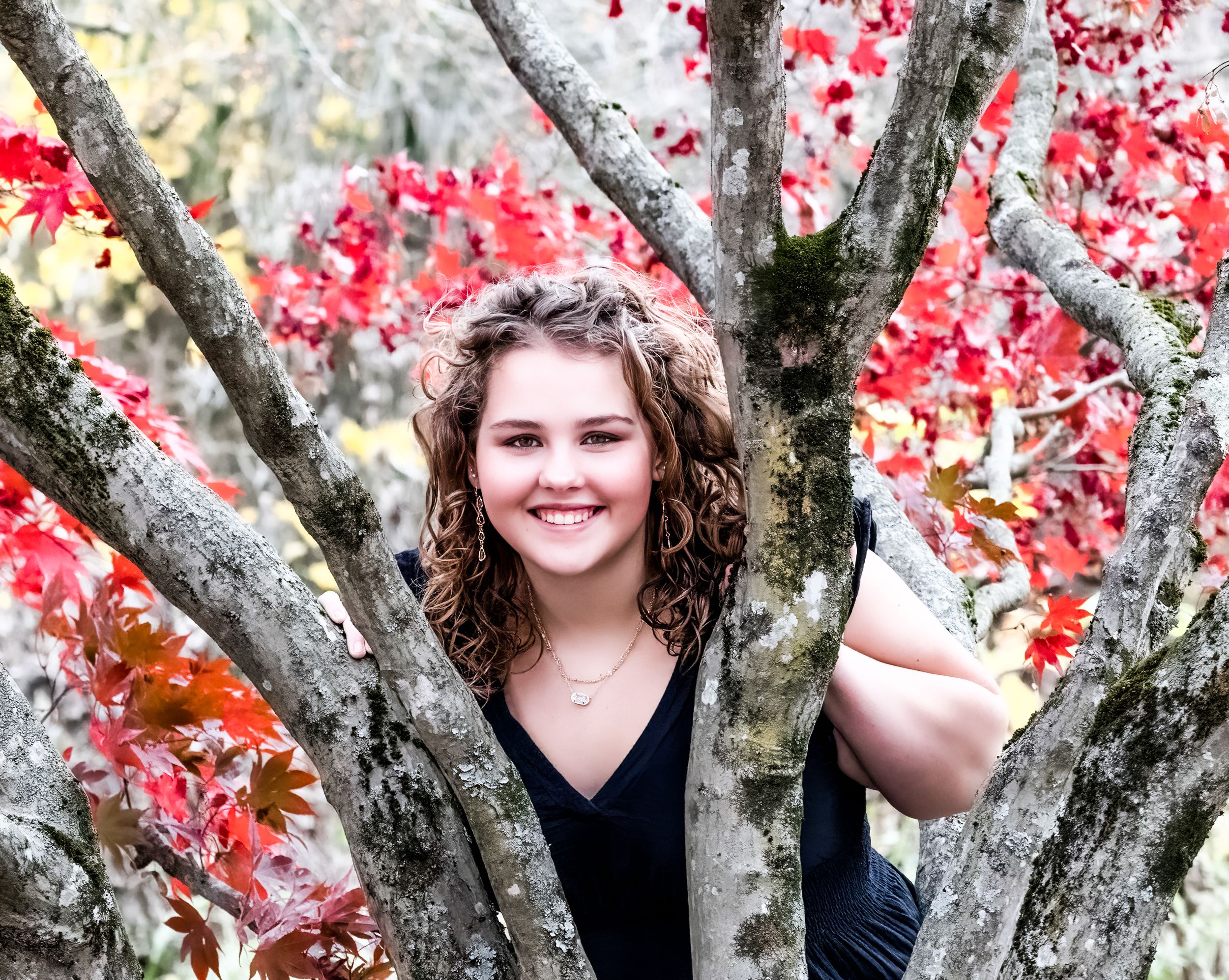 Portrait framed by tree branches with vibrant red autumn foliage.
senior photography