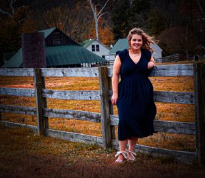 A navy blue dress-clad figure poses by a rustic wooden fence at sunset.
Senior photography