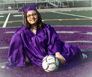 Graduate in purple cap and gown sits on sports field with soccer ball.
senior photography
soccer senior