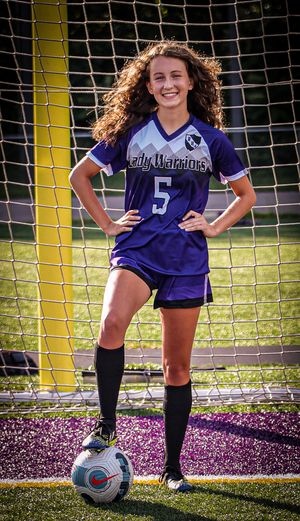 Soccer player in purple jersey poses with ball in front of goal net.
senior photography
soccer senior