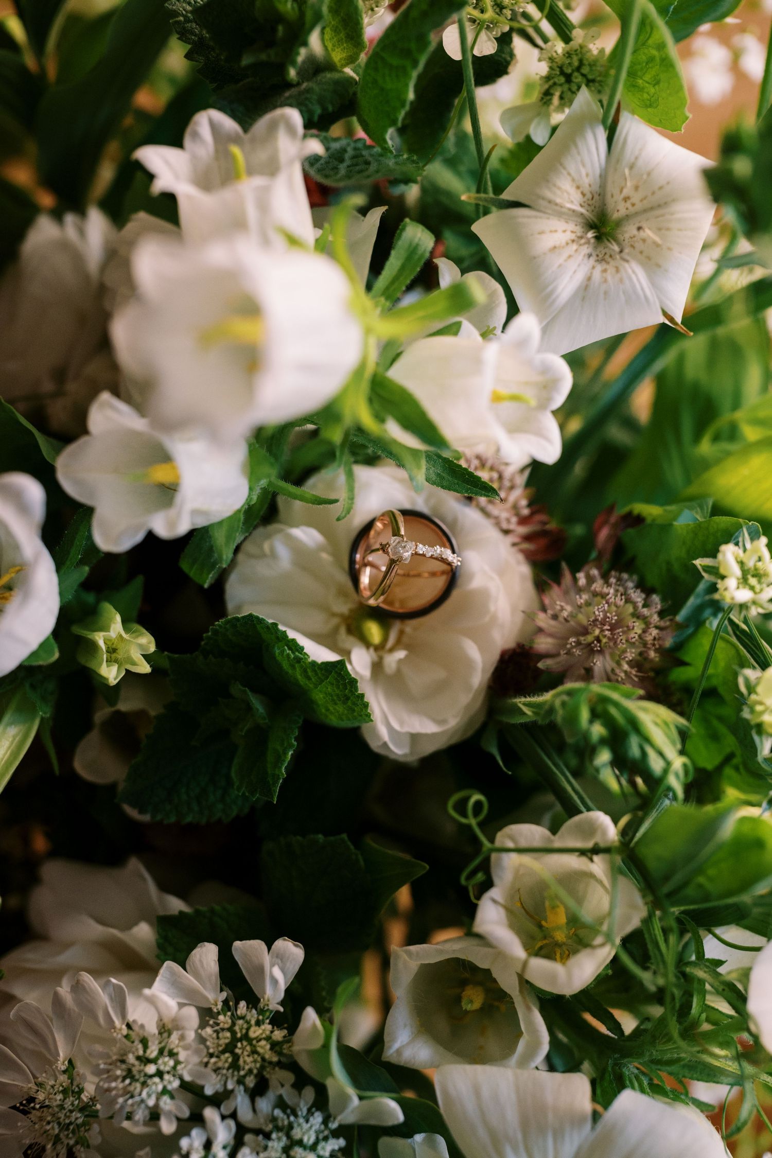 Gold wedding ring nestled among white flowers and green foliage in an elegant floral arrangement.