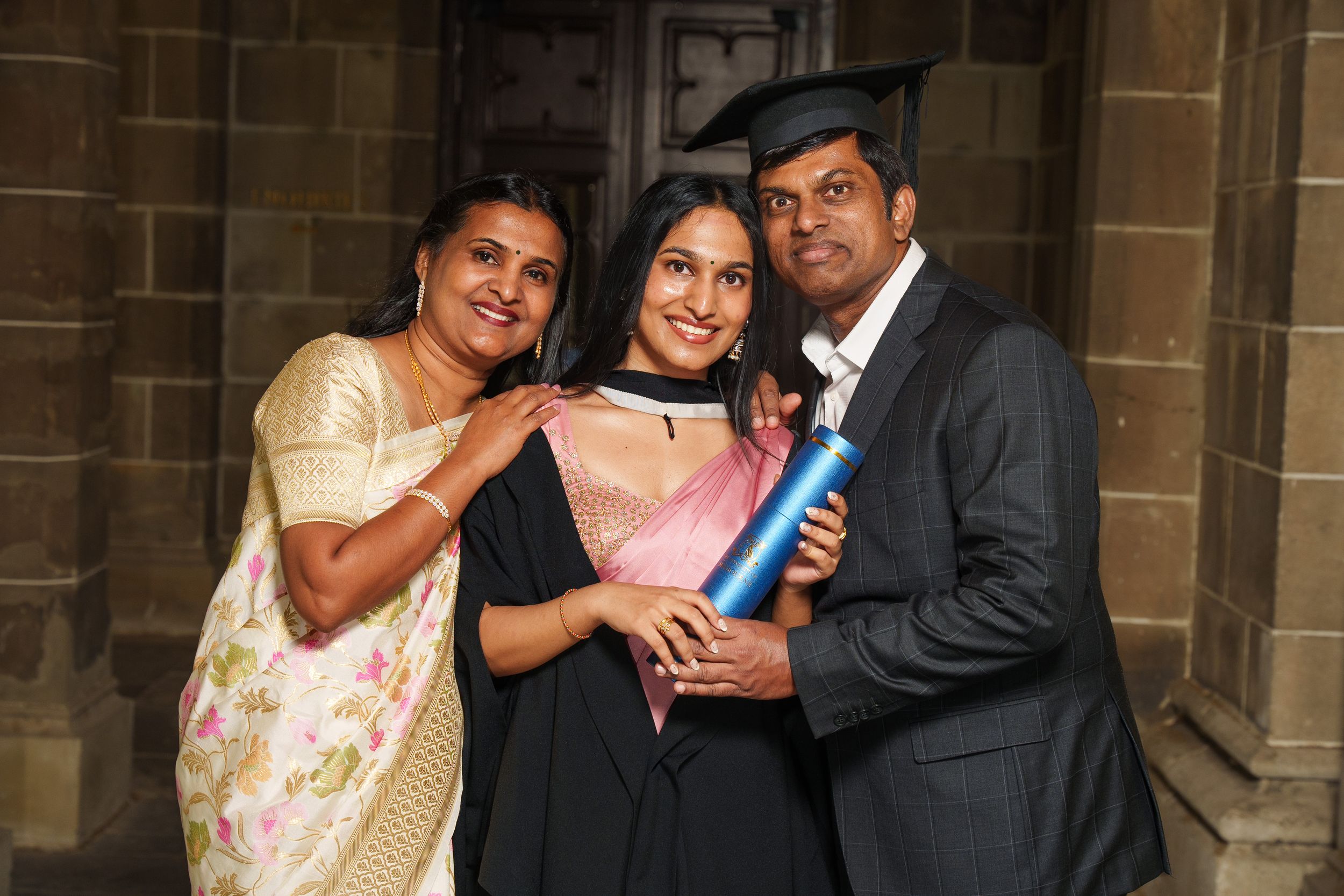 Family celebrates graduation moment in formal attire with diploma.
