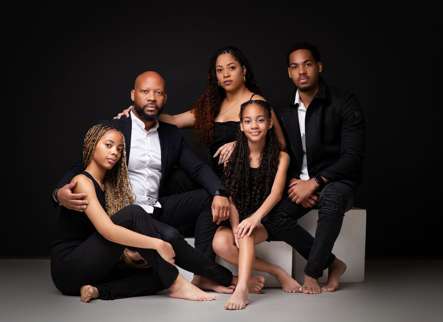 Professional family portrait with coordinated black outfits in studio setting.