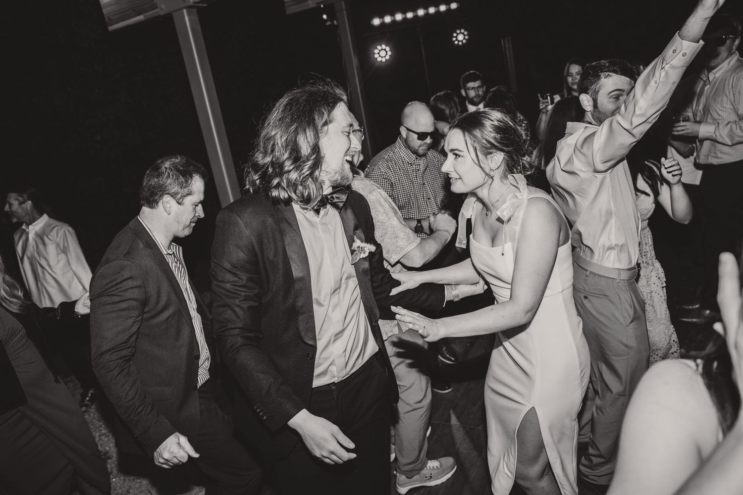 Black and white photo of wedding guests dancing and celebrating at a lively reception.