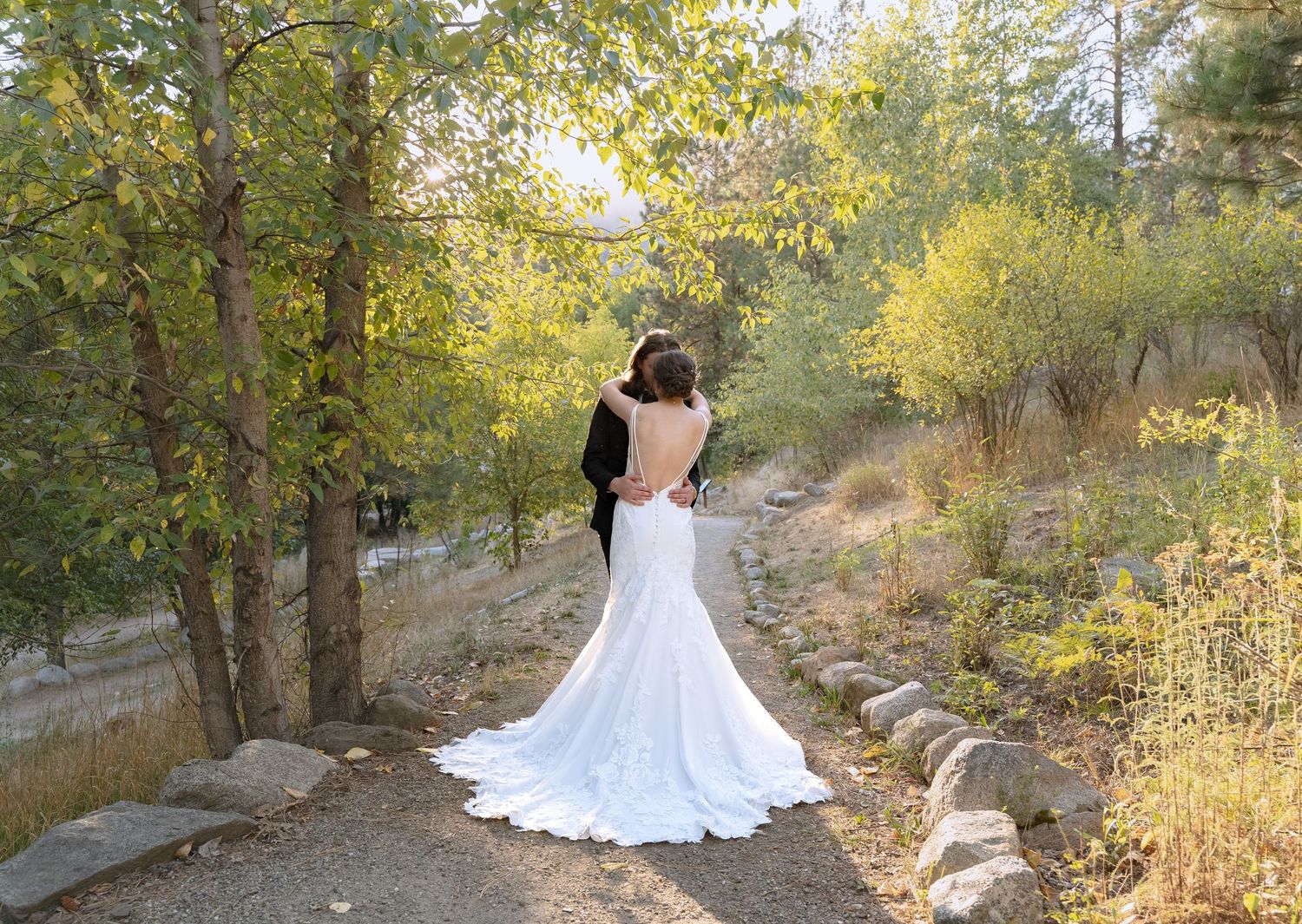 A bride in a flowing white dress poses on a scenic mountain trail surrounded by autumn foliage.