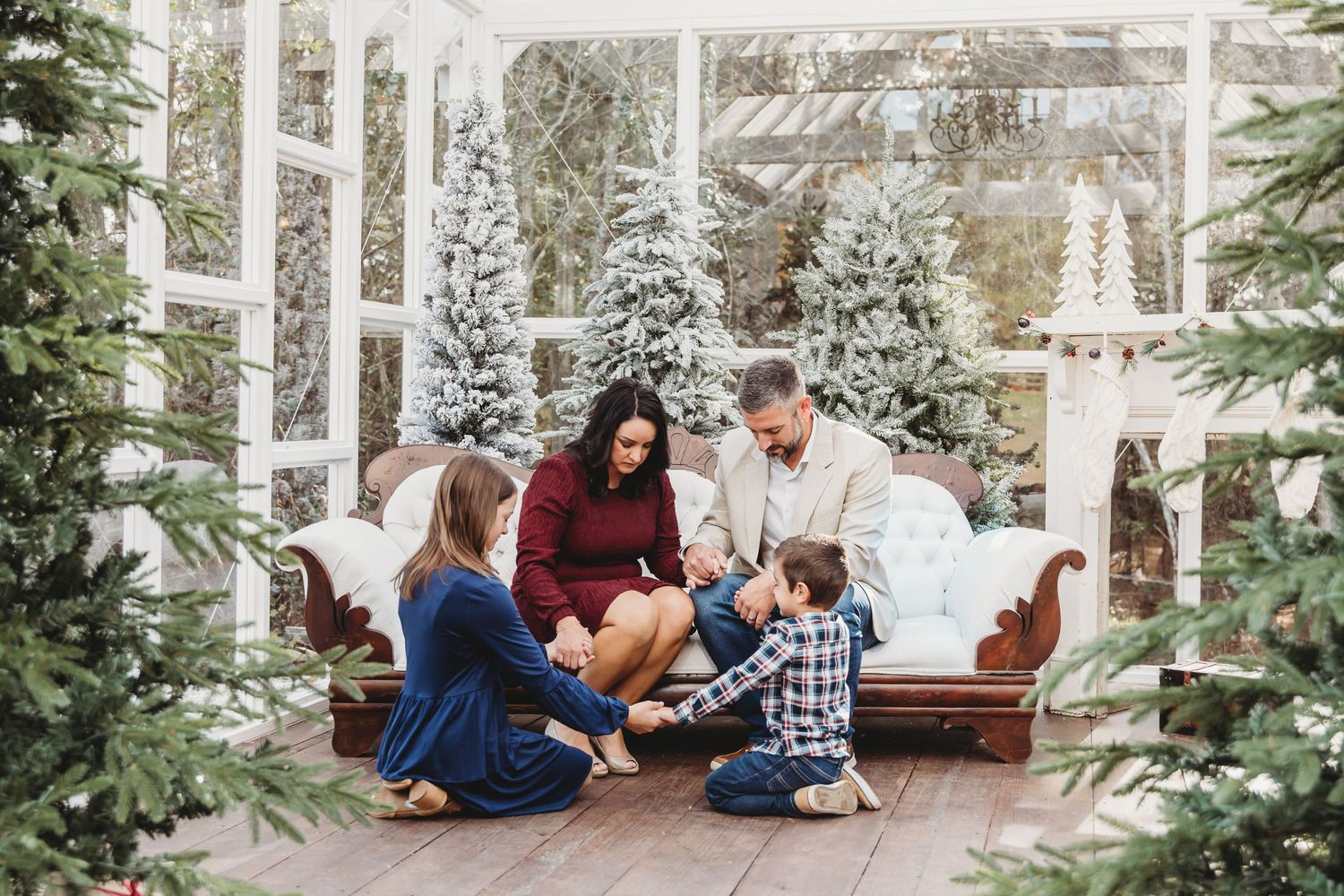 Family lifestyle session in a bright sunroom with white decor and snowy evergreen trees visible outside.