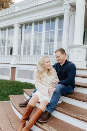 Couple sitting on white colonial building steps wearing casual fall attire.