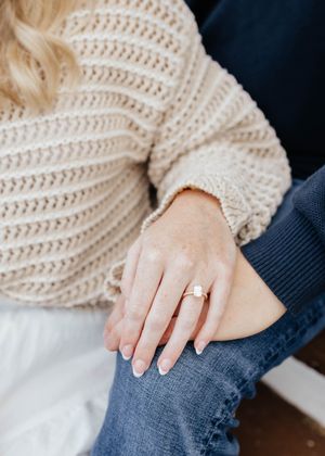 Close up of engagement ring on hand with cream knit sweater and denim background.