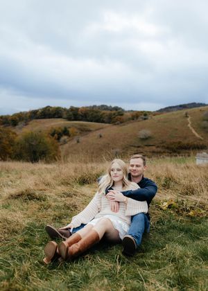 Couple relaxing on grassy hillside during autumn with rolling hills in background.