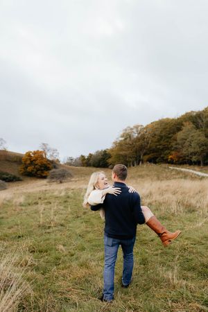 Couple playfully poses together in a scenic autumn field with tall grass and trees.