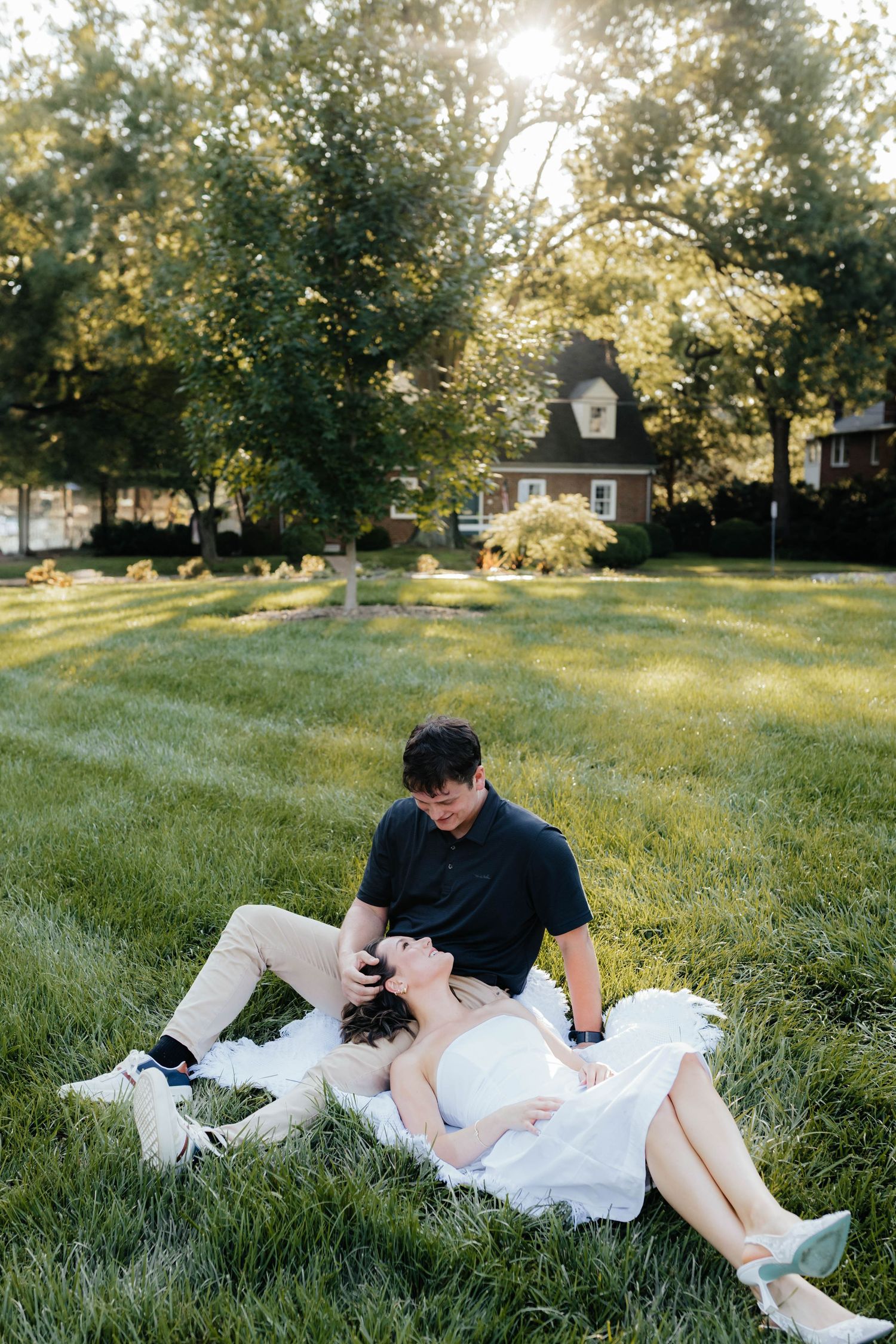 Couple relaxes on grass during sunset photoshoot in casual setting.