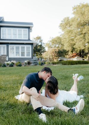 A couple playfully rolls on lush green grass outside a modern house on a sunny day.