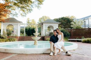 Couple poses near swimming pool with elegant white columns in background.