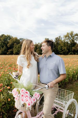 Couple poses with vintage bicycle and pink flowers in blooming wildflower field.