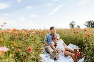Couple relaxes together in a vibrant field of orange wildflowers on a bright summer day.
